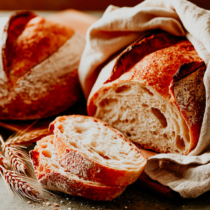 Loaf of bread with a slice cut, wrapped in a cloth on a wooden surface.