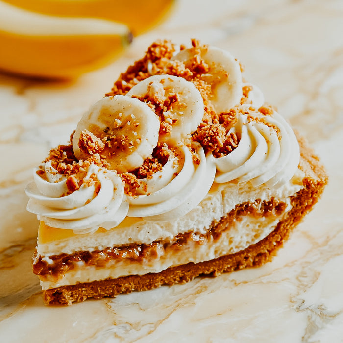 Slice of banana cream pie with whipped cream and crushed cookies on a marble surface