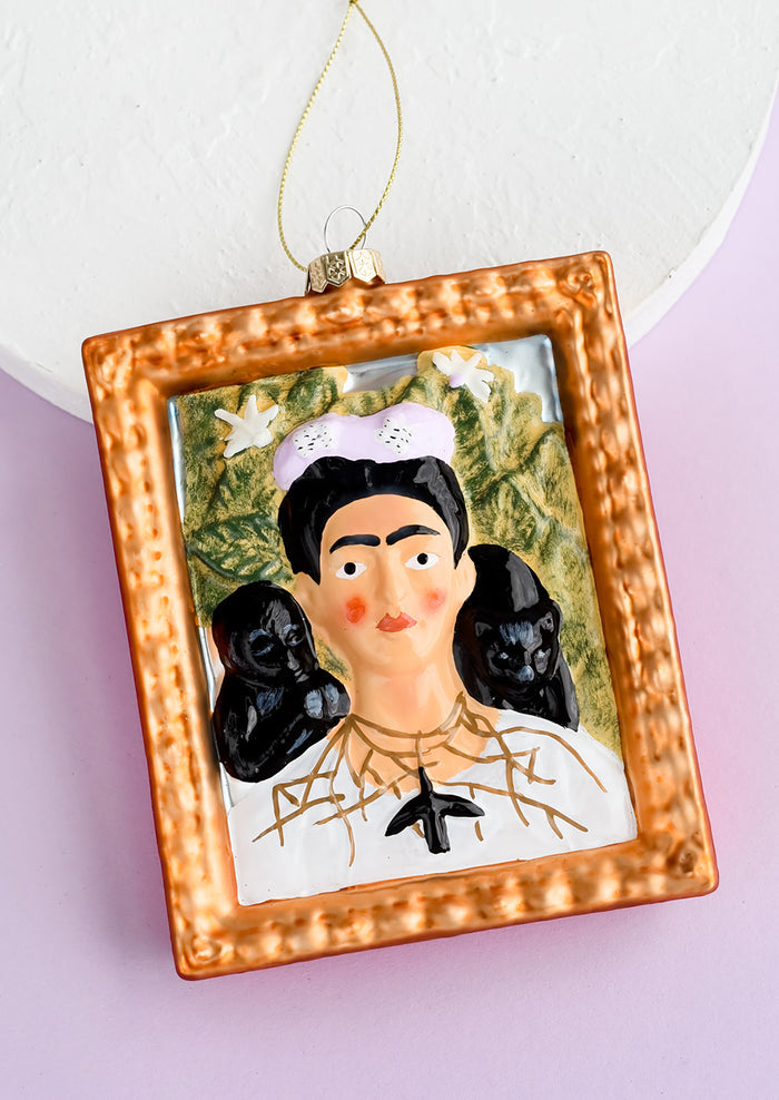 A decorative glass ornament in frame shape with image of Frida Kahlo.