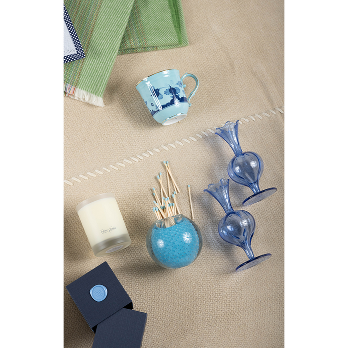 White candle in frosted glass jar, round blue ceramic diffuser with wooden sticks, and two blue glass bird-shaped holders on .