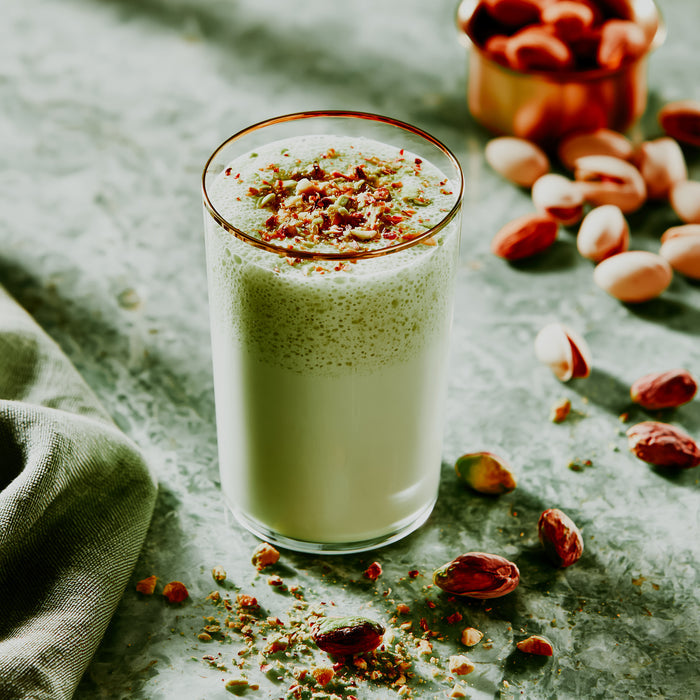 Glass of pistachio milk with nuts on a textured surface