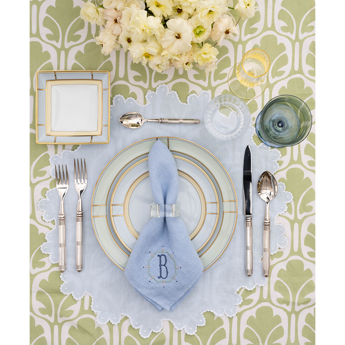Table-setting with green and white tablecloth, green and blue china, and a monogrammed blue napkin.