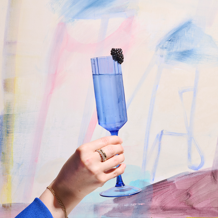 Blue champagne flute with blackberry in front of colorful abstract art.