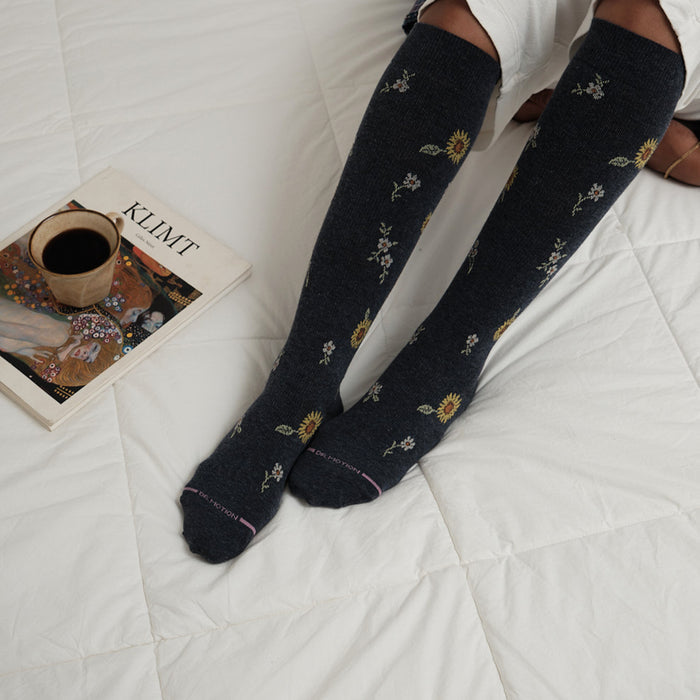 Knee-high compression socks with a floral pattern, featuring sunflowers and small flowers, on a white quilted surface.