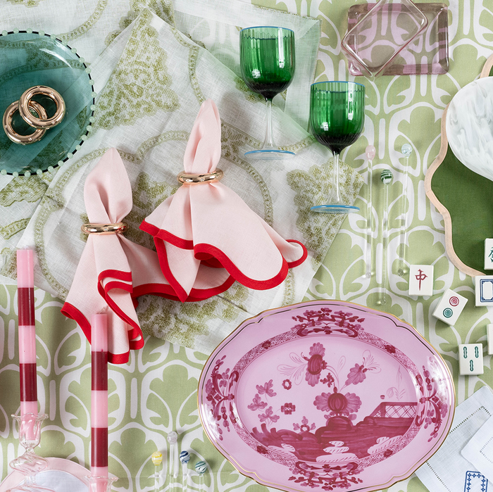 Pink and red cloth napkins tied with gold rings displayed on a green and white patterned tablecloth.