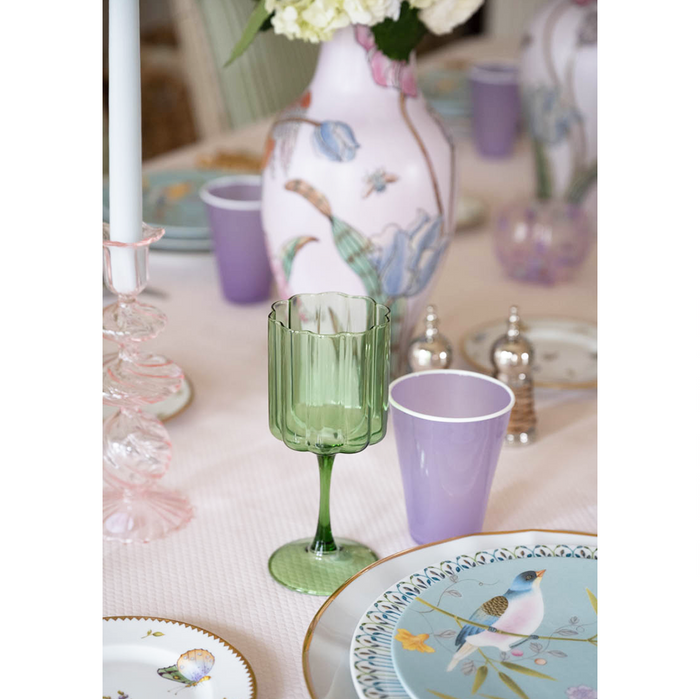close up of a green scalloped  wine glass and purple ceramic water up on a dining table