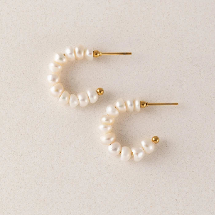 Pearl hoop earrings with gold accents on a light beige background