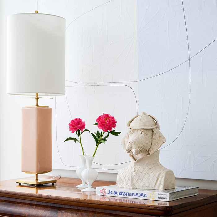 White ceramic bud vase with three curved spouts holding pink flowers on wooden surface.