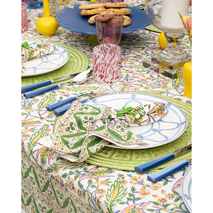 White dinner plate with blue decorative lines on a colorful floral patterned tablecloth, paired with blue-handled cutlery.