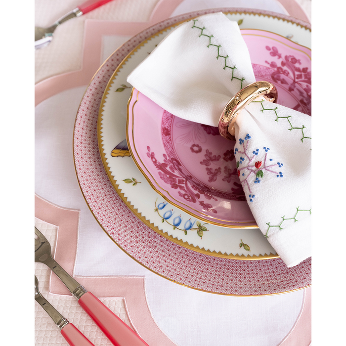 Pink scalloped placemat under decorative pink and white floral plates with a white napkin and gold napkin ring.