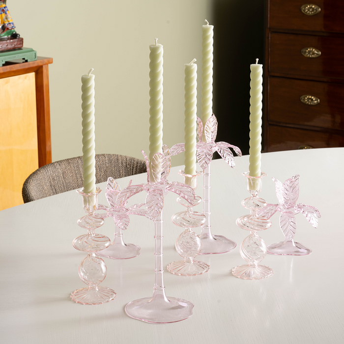 Set of five pink glass candlesticks with twisted and butterfly-shaped designs, each holding a white taper candle.