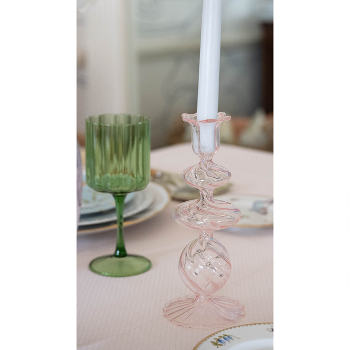 Delicate pink glass candlestick with swirl design holding a white tapered candle.