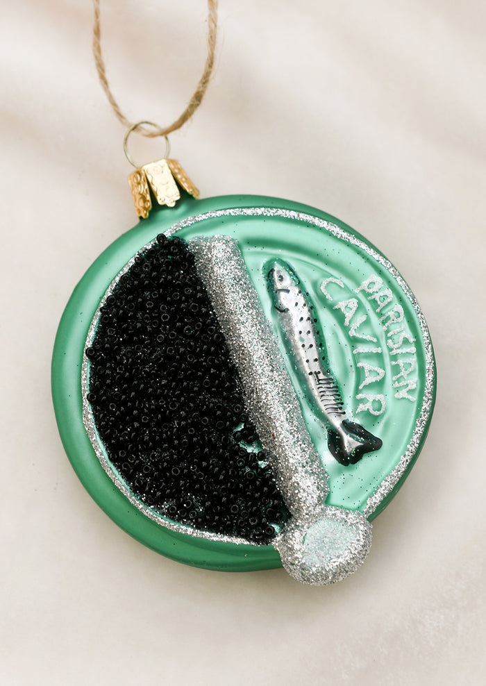 A glass ornament in the shape of round green Parisian caviar tin.