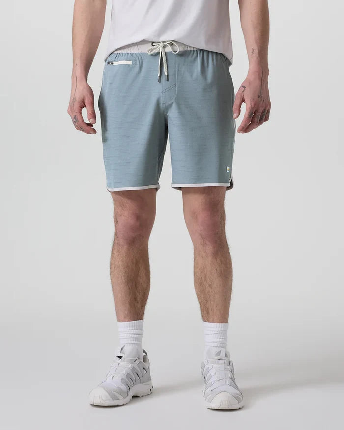A person standing and wearing Vuori Banks Shorts in a gray color with a drawstring waist and a 7-inch inseam.